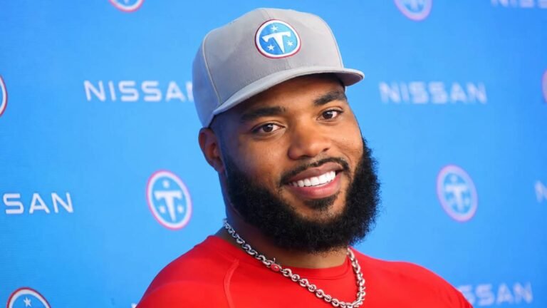 Tennessee Titans defensive tackle Jeffery Simmons smiles confidently while signing his record contract extension at the team facility in Nashville, Titans logo prominent in the background.