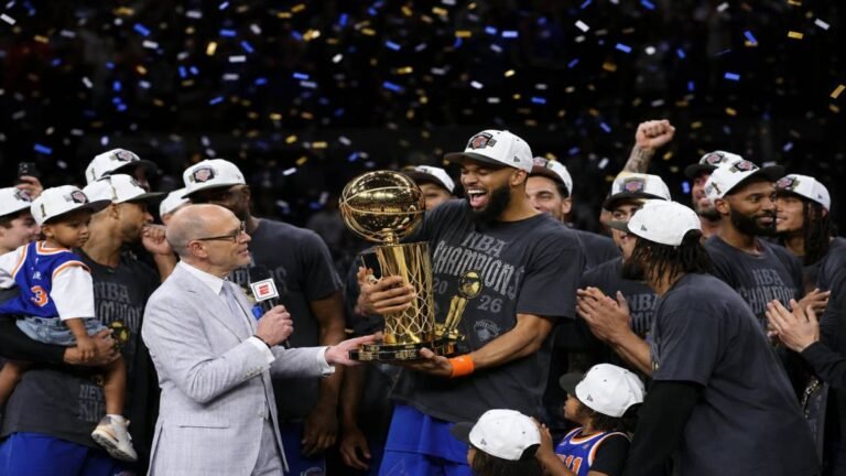 New York Jets players on the field with a large Knicks 2026 NBA Champions banner and trophy graphic in the background, capturing the cross-sport motivation in New York.