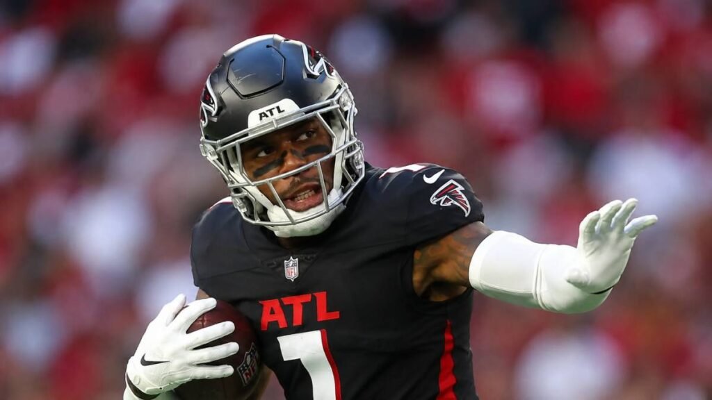 Atlanta Falcons tight end Kyle Pitts celebrates with arms outstretched in his red No. 8 jersey under bright stadium lights, capturing the energy and promise of his new long-term contract extension.