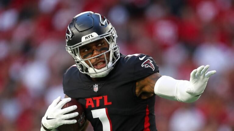 Atlanta Falcons tight end Kyle Pitts celebrates with arms outstretched in his red No. 8 jersey under bright stadium lights, capturing the energy and promise of his new long-term contract extension.