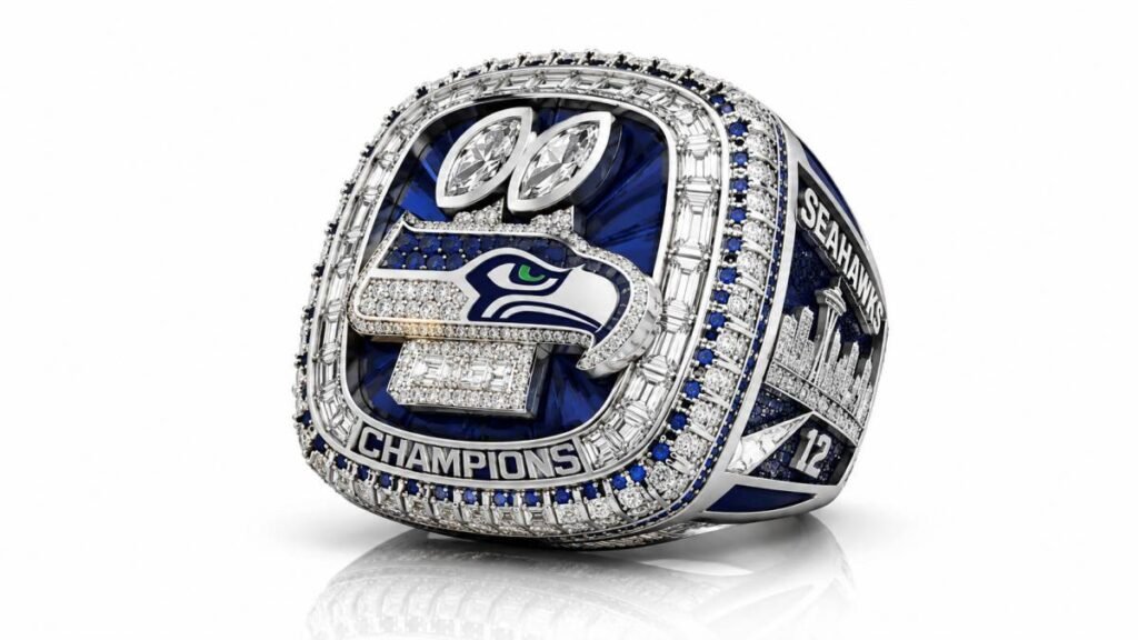 Close-up of the Seattle Seahawks Super Bowl LX championship ring showing the central logo, blue sapphires, 50 diamonds, and two Lombardi Trophy replicas.
