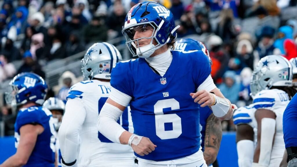 New York Giants QB Jaxson Dart scrambling during a 2026 game as coach John Harbaugh observes intently from the sideline.