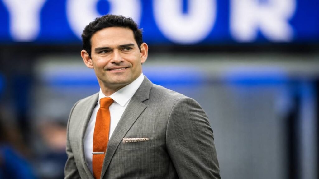 Professional headshot of former NFL quarterback and sports analyst Mark Sanchez wearing a dark suit and tie against a neutral background.