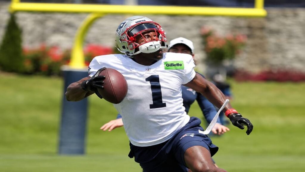 Drake Maye throws a pass to A.J. Brown during a sunny Patriots football camp practice in Foxborough, with young campers and coaches watching in the background.
