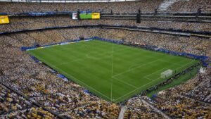 Wide view of the temporary natural grass pitch installed at MetLife Stadium for the 2026 FIFA World Cup final, with empty stands and bright sunlight highlighting the green surface.