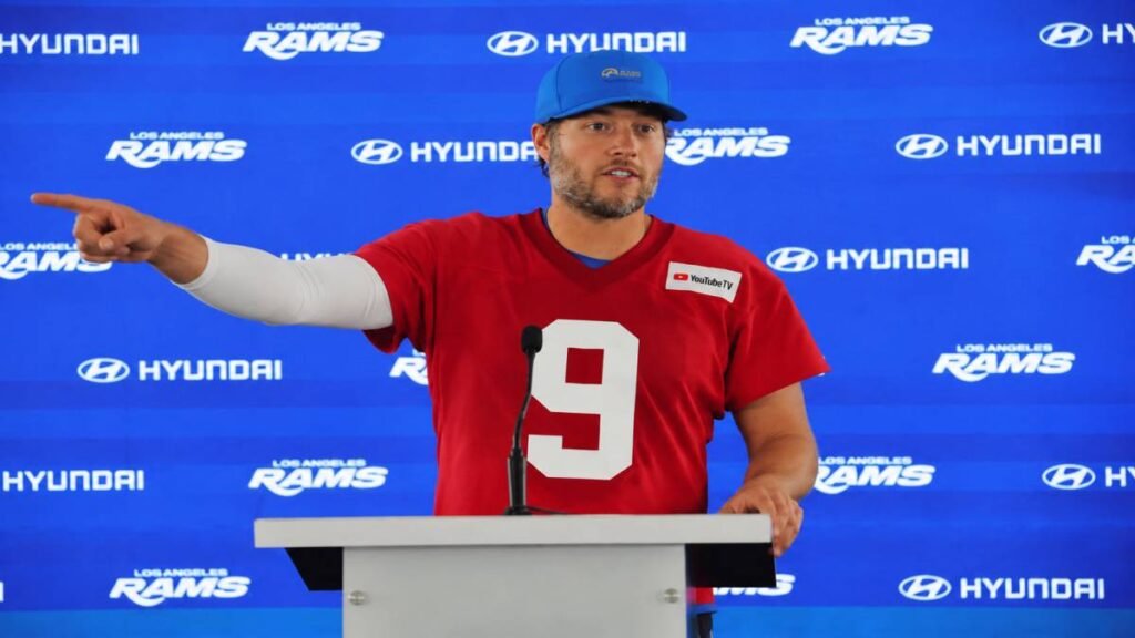 Los Angeles Rams quarterback Matthew Stafford in blue and gold uniform standing on SoFi Stadium field with floating golden dollar signs symbolizing NFL salary cap spending in 2026.