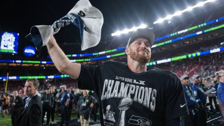 Seattle Seahawks head coach Mike Macdonald and quarterback Sam Darnold stand on the Lumen Field sidelines with the roaring 12s crowd behind them under dramatic lights, capturing the intensity of their Super Bowl-winning campaign.