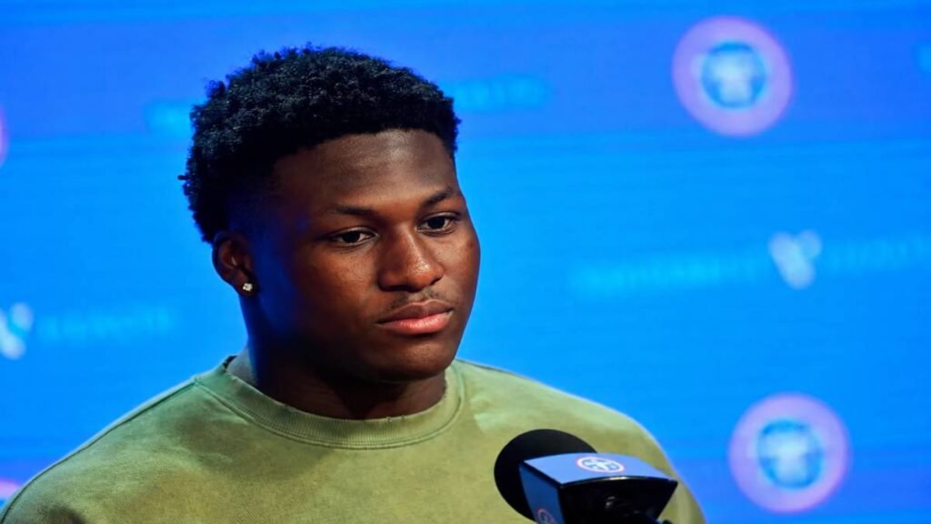Anthony Hill Jr. stands at the podium on 2026 NFL Draft night after the Tennessee Titans selected the Texas linebacker, with Titans branding, an excited crowd, and subtle Texas Longhorns accents in the background.