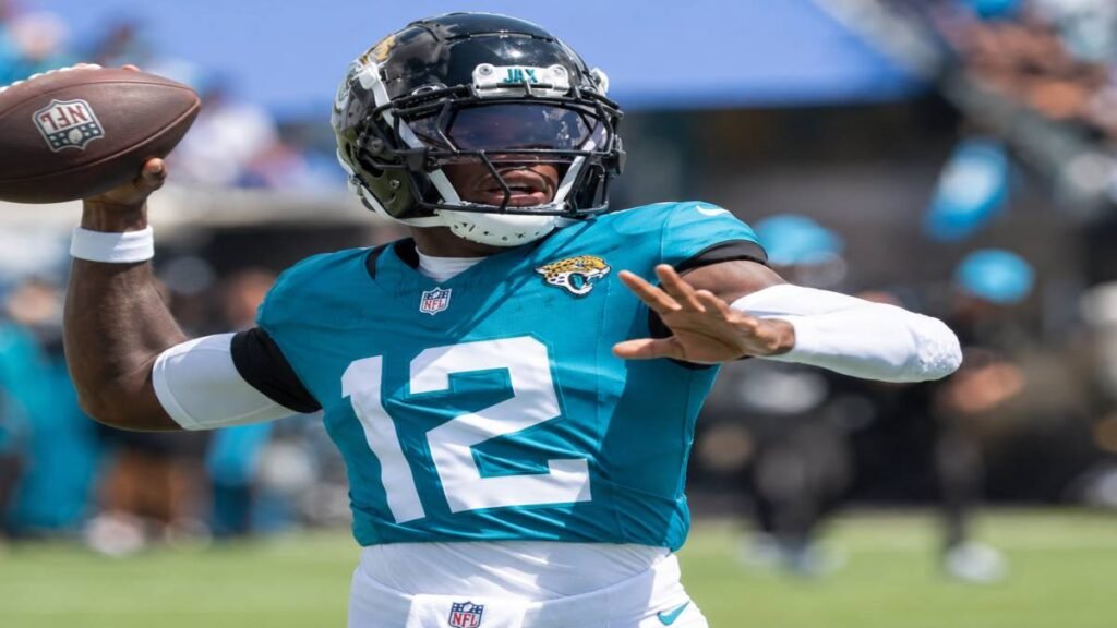 Dynamic action image of Jacksonville Jaguars two-way player Travis Hunter in teal uniform making a one-handed catch on offense with a split view of him breaking up a pass on defense, intense focus, crowded NFL stadium background, 2026 season energy.