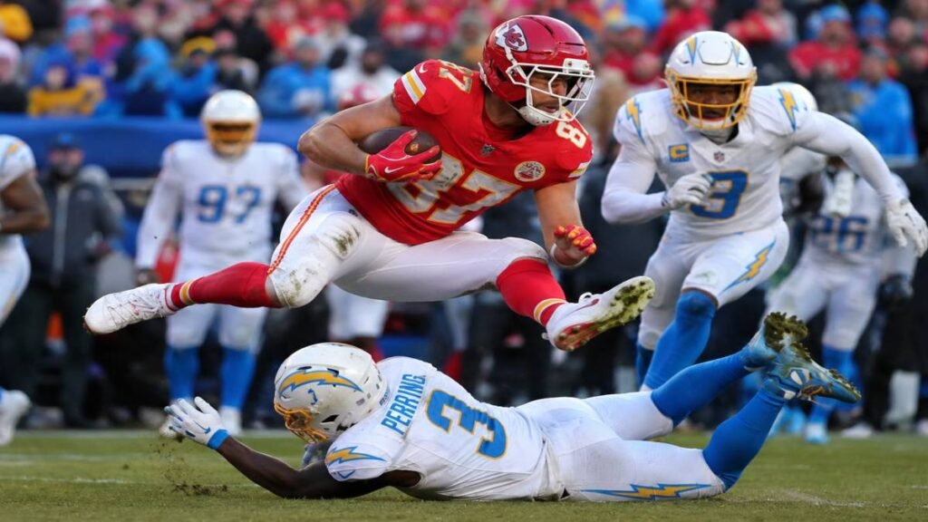 Travis Kelce in full Kansas City Chiefs uniform making a dynamic catch during a 2026 NFL game with fans cheering in the background.