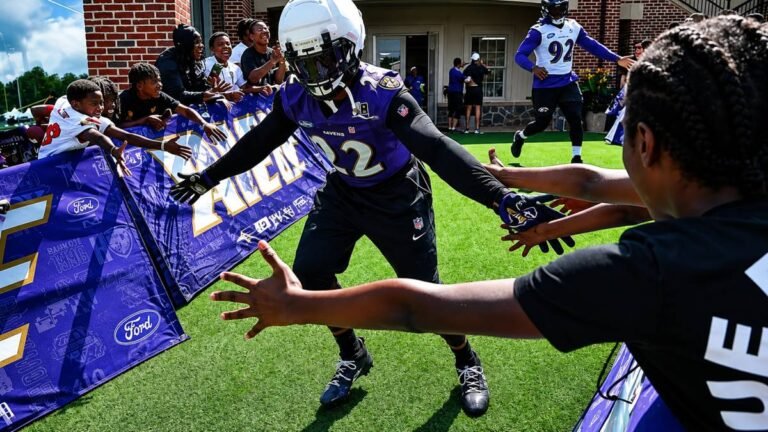 NFL players in full pads practicing during 2026 training camp as fans watch from the sidelines.