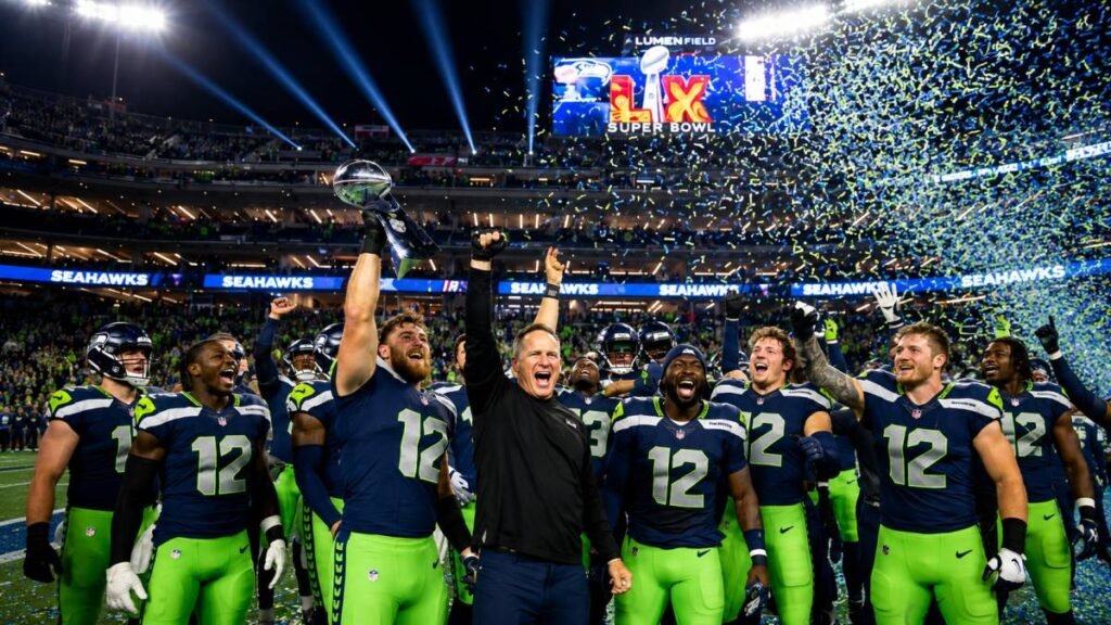 Seattle Seahawks players in navy and green uniforms celebrate Super Bowl LX victory by raising the Vince Lombardi Trophy amid blue and green confetti at Levi's Stadium.